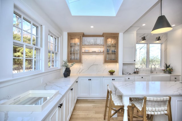 kitchen with glass insert cabinets, a skylight, decorative backsplash, and light stone countertops