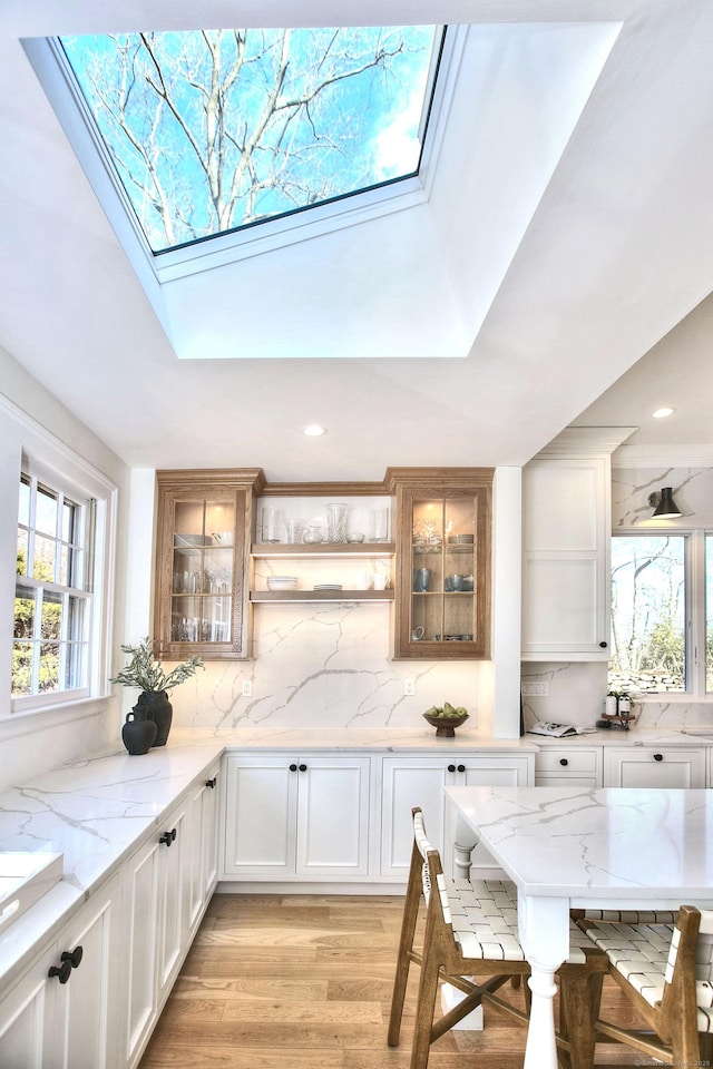 interior space with light wood-style floors, a skylight, glass insert cabinets, and decorative backsplash