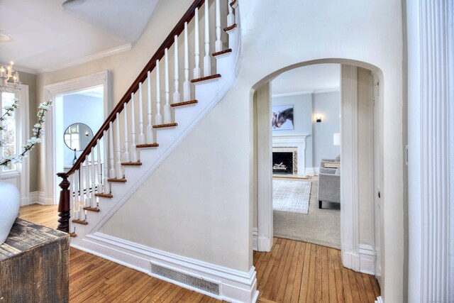 stairway with arched walkways, hardwood / wood-style flooring, visible vents, and crown molding