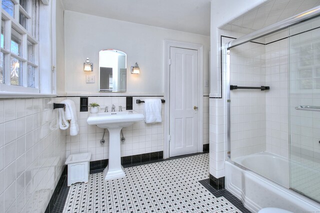 full bathroom with tile patterned flooring, enclosed tub / shower combo, tile walls, and wainscoting