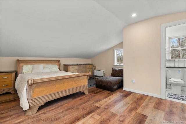 bedroom with hardwood / wood-style flooring, connected bathroom, vaulted ceiling, and heating unit