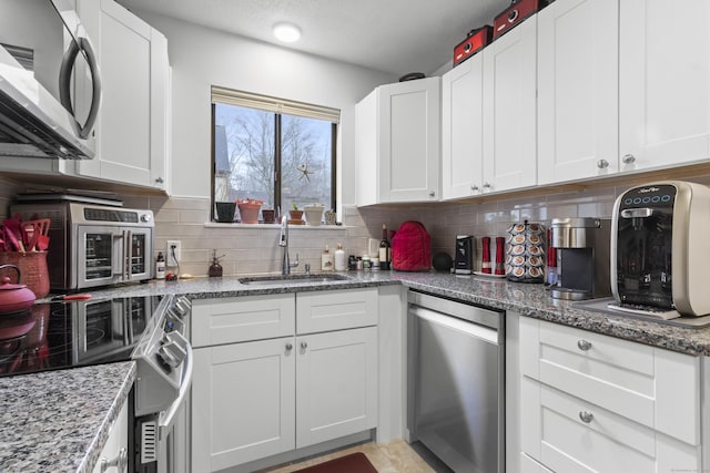 kitchen featuring appliances with stainless steel finishes, white cabinetry, sink, dark stone countertops, and backsplash