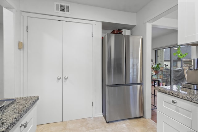 kitchen featuring dark stone countertops, stainless steel fridge, and white cabinets