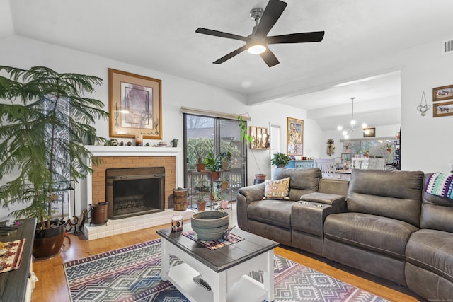 living room featuring wood-type flooring, a brick fireplace, and ceiling fan with notable chandelier