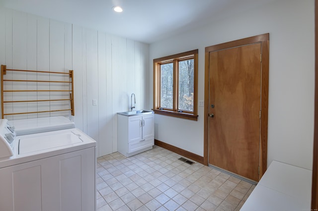 clothes washing area with sink, washing machine and dryer, and cabinets