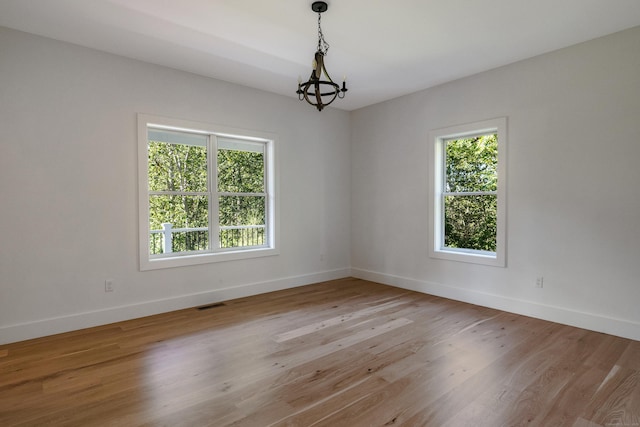 empty room featuring an inviting chandelier and light hardwood / wood-style flooring