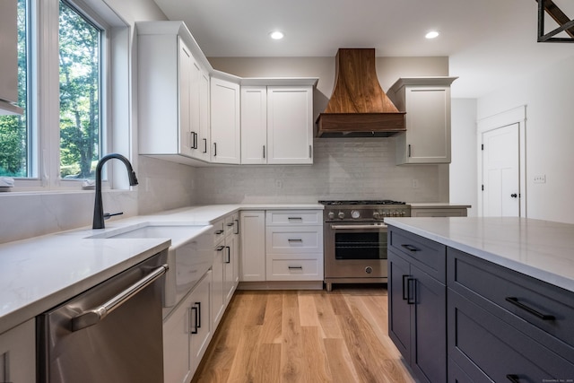 kitchen featuring premium range hood, white cabinetry, light hardwood / wood-style flooring, appliances with stainless steel finishes, and light stone countertops