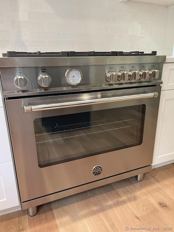 room details with tasteful backsplash, light hardwood / wood-style flooring, high end stainless steel range oven, and white cabinets