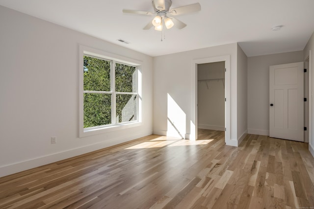 unfurnished bedroom featuring a spacious closet, light hardwood / wood-style floors, a closet, and ceiling fan