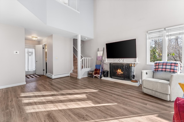 living room featuring a towering ceiling, wood-type flooring, and a baseboard heating unit