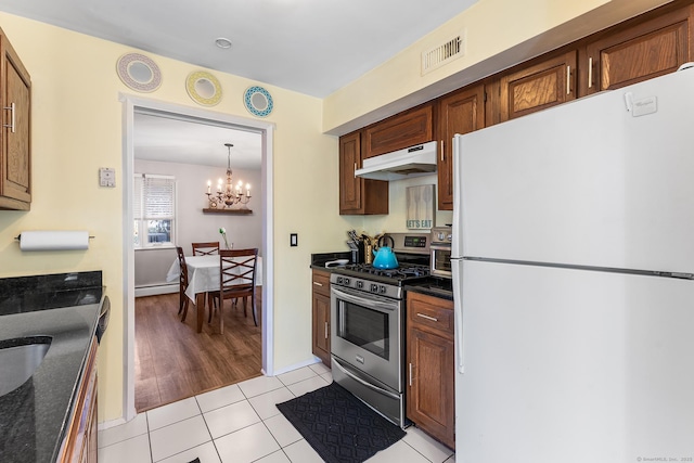 kitchen with a chandelier, light tile patterned floors, white refrigerator, baseboard heating, and stainless steel range with gas stovetop