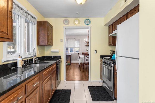 kitchen featuring stainless steel gas stove, black dishwasher, sink, white refrigerator, and light tile patterned floors