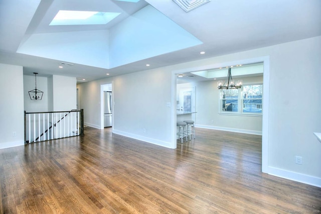 unfurnished living room featuring an inviting chandelier, dark hardwood / wood-style floors, and lofted ceiling with skylight