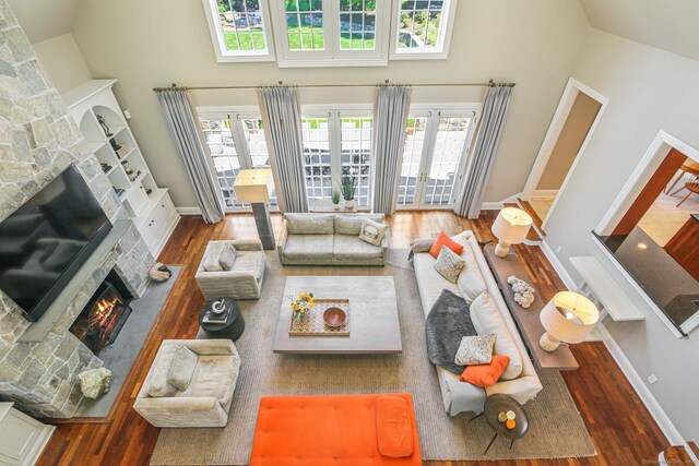 living room featuring dark wood-type flooring, a towering ceiling, and a stone fireplace