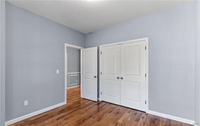 unfurnished bedroom featuring wood finished floors, a closet, and baseboards