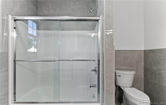 bathroom featuring a shower with shower door, tile walls, and toilet