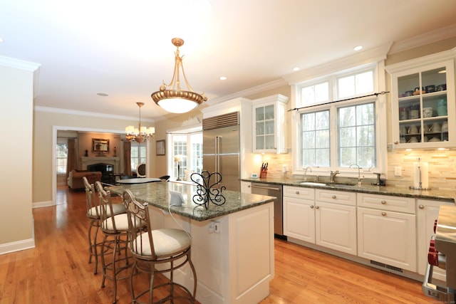 kitchen with white cabinetry, decorative light fixtures, appliances with stainless steel finishes, a kitchen island, and dark stone counters