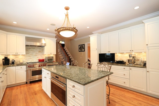 kitchen featuring white cabinetry, dark stone countertops, appliances with stainless steel finishes, a kitchen island, and wall chimney range hood