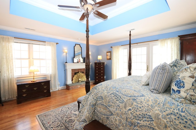 bedroom featuring ornamental molding, ceiling fan, a tray ceiling, a brick fireplace, and light hardwood / wood-style flooring