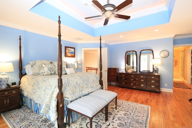 bedroom with crown molding, light hardwood / wood-style flooring, and a tray ceiling