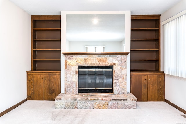 living room featuring a stone fireplace, built in shelves, and carpet