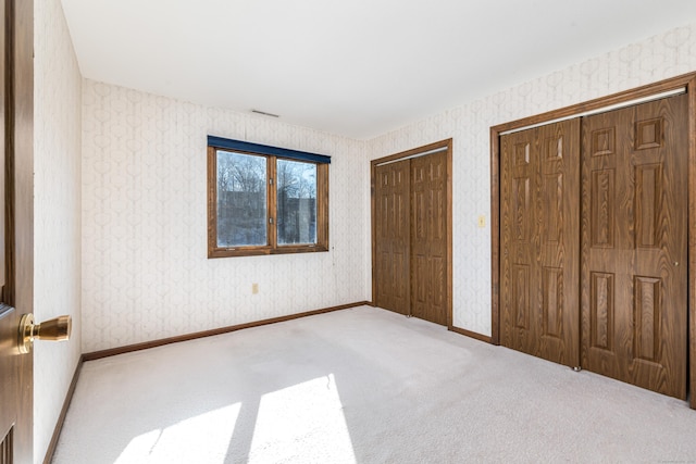 unfurnished bedroom featuring two closets and light colored carpet