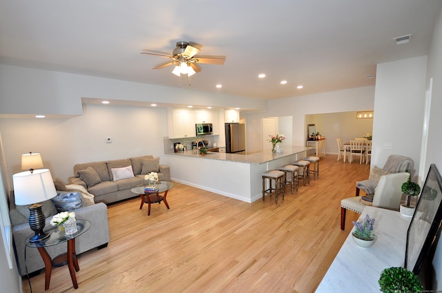 living room featuring ceiling fan, sink, and light hardwood / wood-style flooring