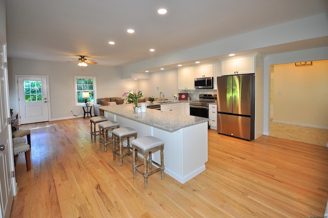 kitchen with appliances with stainless steel finishes, tasteful backsplash, white cabinetry, a kitchen bar, and light wood-type flooring