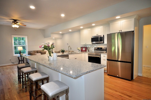 kitchen featuring appliances with stainless steel finishes, sink, white cabinets, a kitchen bar, and light hardwood / wood-style flooring