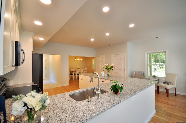 kitchen with sink, white cabinets, light stone counters, black appliances, and light wood-type flooring