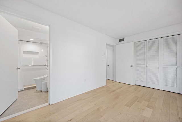 unfurnished bedroom featuring ensuite bath, a closet, and light wood-type flooring