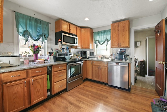 kitchen with sink, backsplash, stainless steel appliances, a textured ceiling, and light wood-type flooring