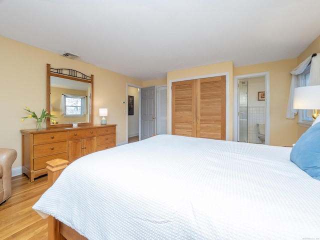 bedroom with two closets, ensuite bathroom, and light wood-type flooring