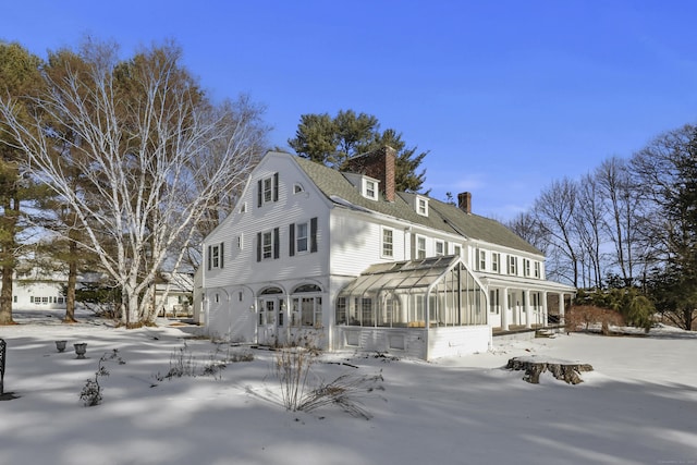 snow covered back of property featuring a sunroom