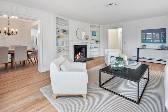 living room featuring built in shelves, an inviting chandelier, baseboard heating, and light hardwood / wood-style flooring