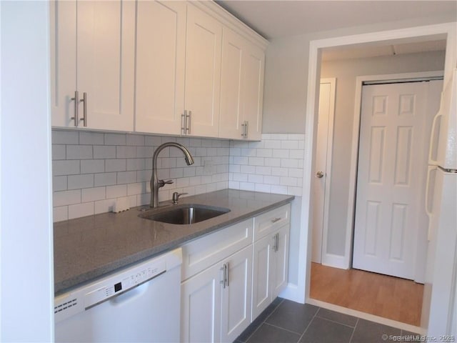 kitchen with sink, white appliances, white cabinetry, dark tile patterned flooring, and dark stone counters