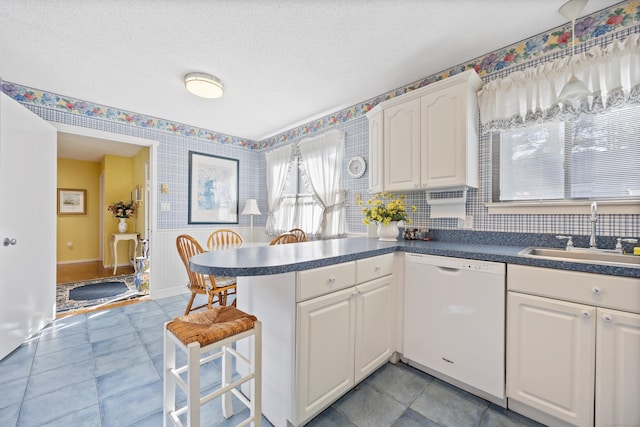 kitchen with sink, a textured ceiling, white dishwasher, kitchen peninsula, and white cabinets