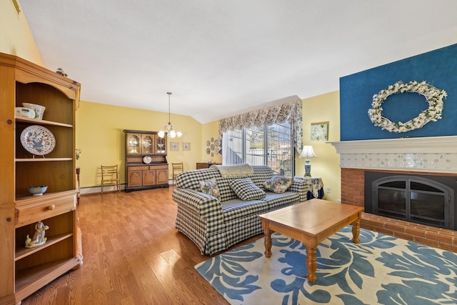 living room featuring wood-type flooring, lofted ceiling, a notable chandelier, baseboard heating, and a brick fireplace