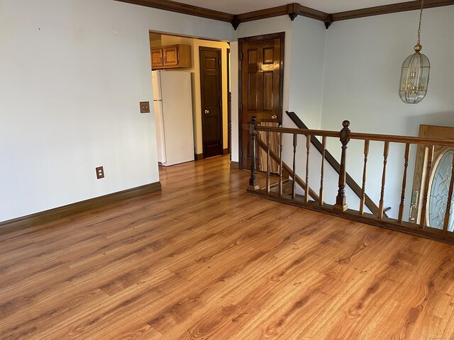 empty room with baseboards, a notable chandelier, wood finished floors, and crown molding