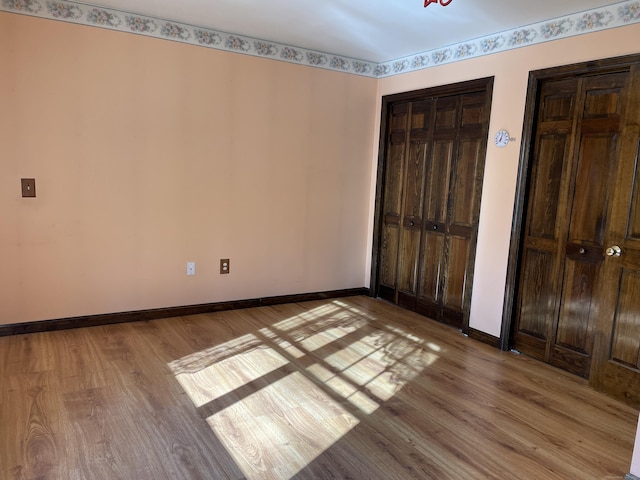 unfurnished bedroom featuring baseboards, two closets, and wood finished floors