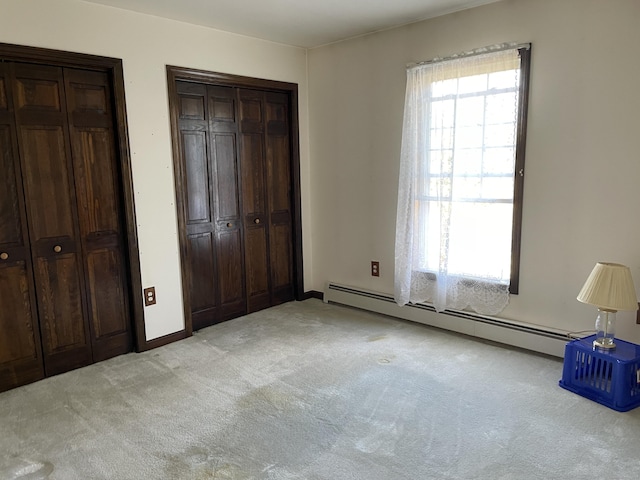 unfurnished bedroom with light colored carpet, multiple closets, and baseboard heating