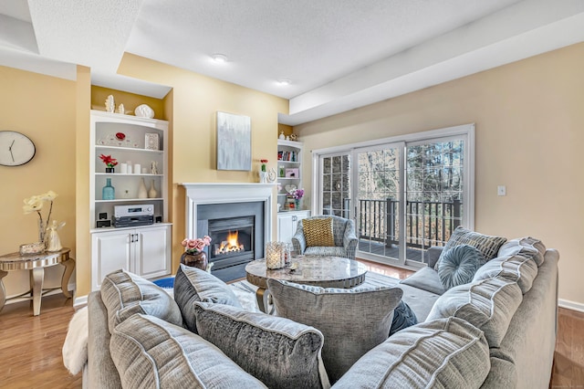 living room with built in shelves, light hardwood / wood-style floors, and a textured ceiling