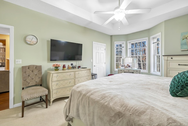 bedroom with a tray ceiling, light colored carpet, and ceiling fan