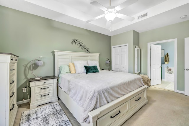 bedroom featuring light colored carpet, ceiling fan, a raised ceiling, ensuite bath, and a closet