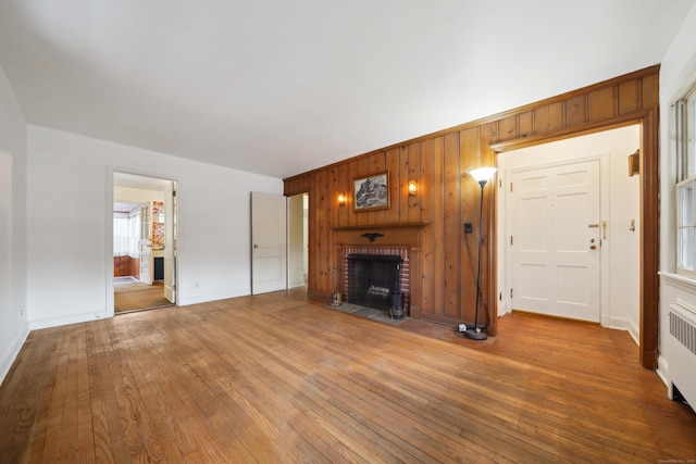 unfurnished living room with hardwood / wood-style flooring, wooden walls, radiator, and a fireplace