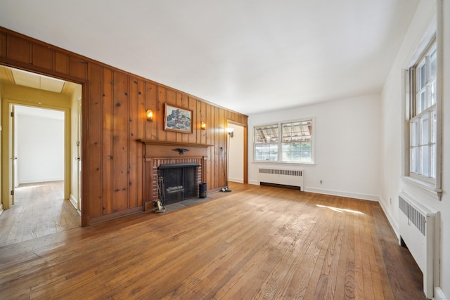 unfurnished living room featuring hardwood / wood-style flooring, radiator heating unit, a fireplace, and wood walls