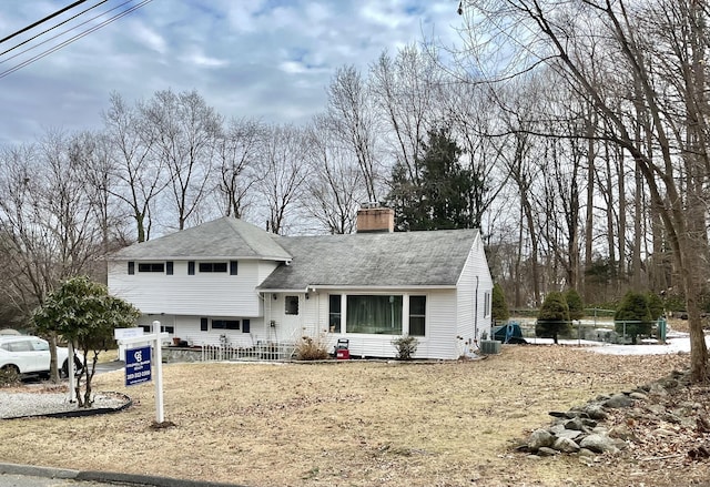 split level home with central AC, fence, and a chimney