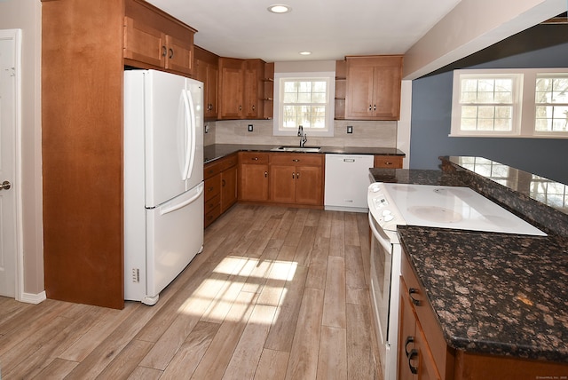 kitchen featuring sink, dark stone countertops, white appliances, light hardwood / wood-style floors, and decorative backsplash