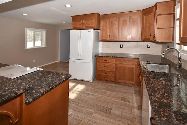 kitchen featuring sink, light hardwood / wood-style flooring, white refrigerator, dark stone counters, and backsplash