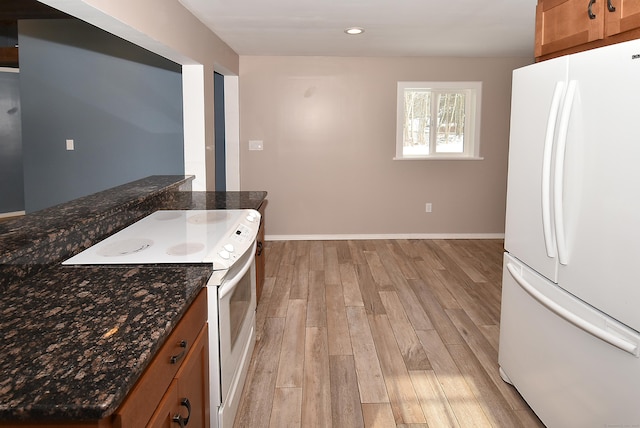 kitchen with dark stone countertops, white appliances, and light wood-type flooring